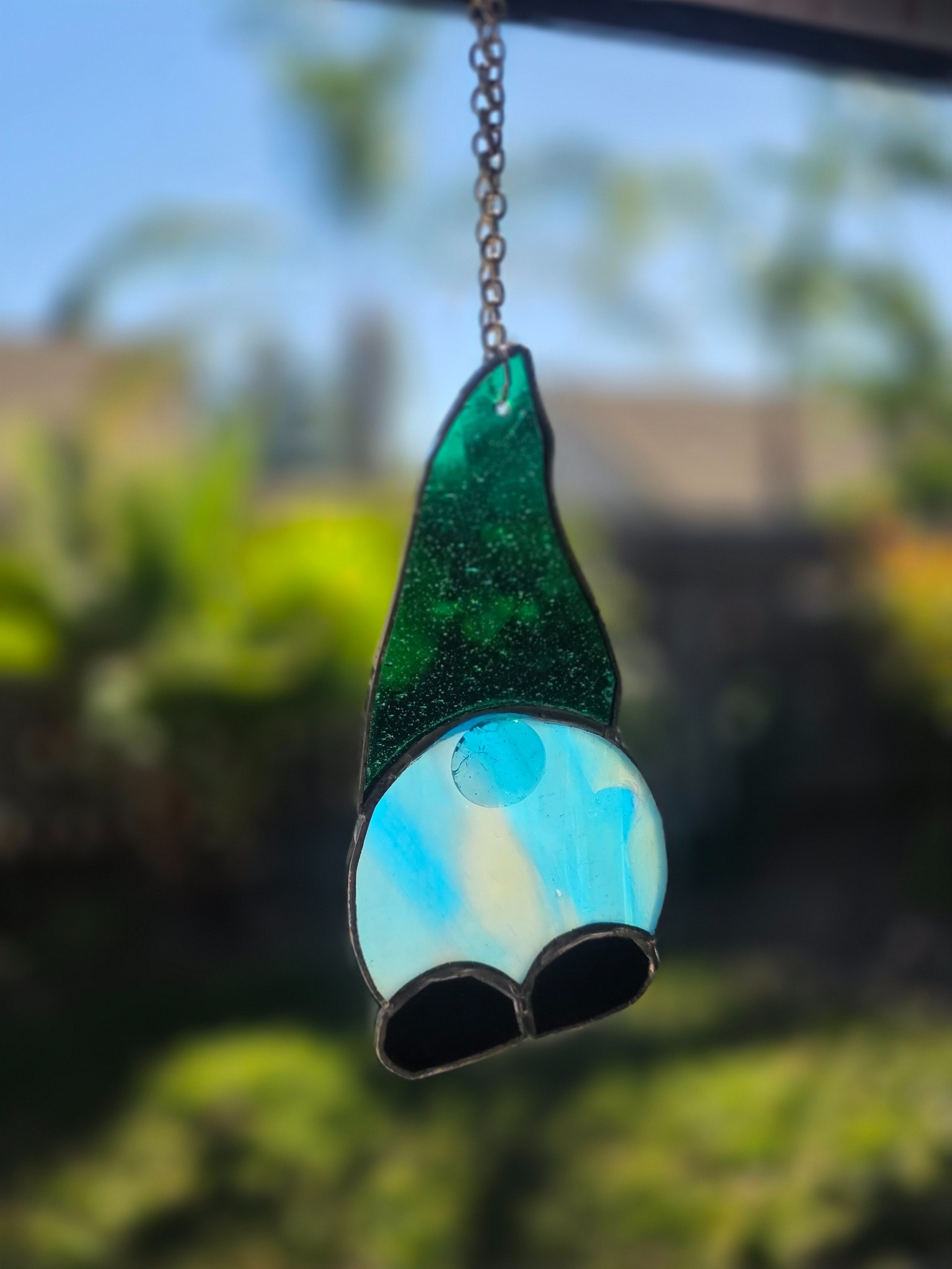 One-of-a-kind green and blue stained-glass gnome hanging in a sunny window